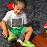 Alexander joined the competition — help win amazing prizes! ball, bun, carpet, casual_clothing, child, face, green_shorts, hair, indoors, playroom, portrait, shoes, sitting, smiling, sneakers, t_shirt, toddler, toy_truck, toys, wood_floor