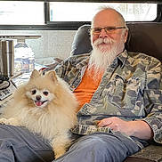 Ozzy is registered to the contest to win money with this photo: man, dog, pomeranian, beard, glasses, camouflage_shirt, orange_tshirt, indoor, window, blinds, chair, smile, happy, pet, fluffy_dog, relaxing, seated, laptop, water_bottle, cozy
