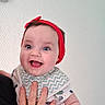 adult_hand, baby, bib, blue_eyes, child, clothing, cute, expression, face, hand, happy, headband, indoor, infant, person, portrait, skin, smile, texture, white_wall