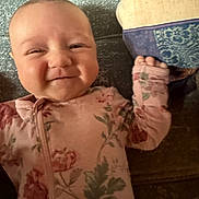 Nevaeh is registered to the contest to win money with this photo: baby, infant, smile, face, floral_onesie, couch, pillow, hand, cheeks, head, clothing, pattern, texture, indoor, child, cute, happy, portrait, lying_down, cozy