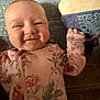 baby, infant, smile, face, floral_onesie, couch, pillow, hand, cheeks, head, clothing, pattern, texture, indoor, child, cute, happy, portrait, lying_down, cozy
