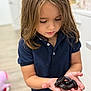 child, girl, kid, snake, black_snake, reptile, hands, holding, indoor, portrait, close_up, long_hair, navy_shirt, curious, eyelashes, home, wood_floor, shallow_depth_of_field, toy_or_pet, person