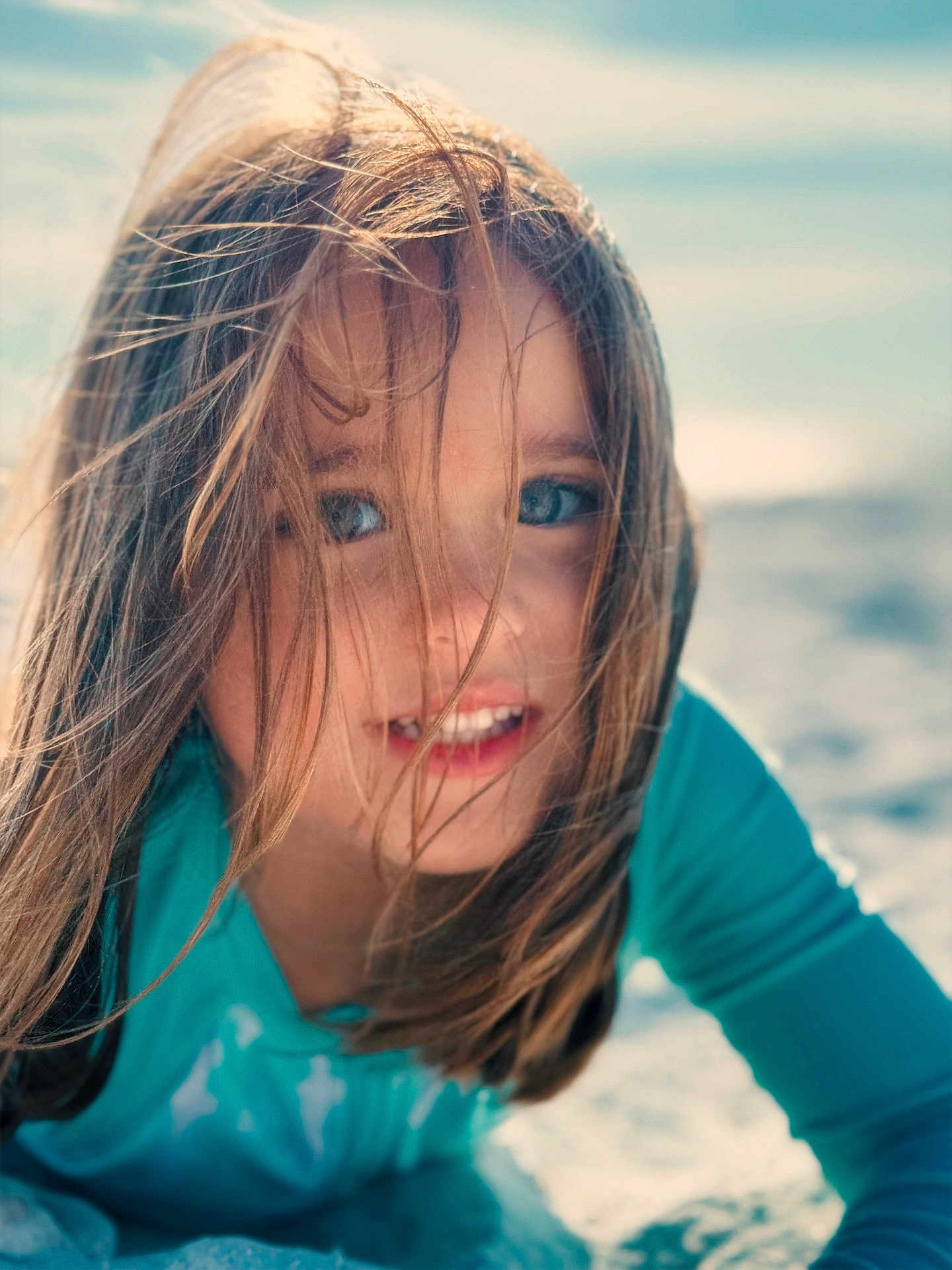 Megan is registered to the contest to win money with this photo: child, girl, smile, face, hair, windblown, blue_eyes, closeup, portrait, beach, sand, outdoor, sunlight, candid, happy, long_hair, turquoise_shirt, playful, emotive, young_person