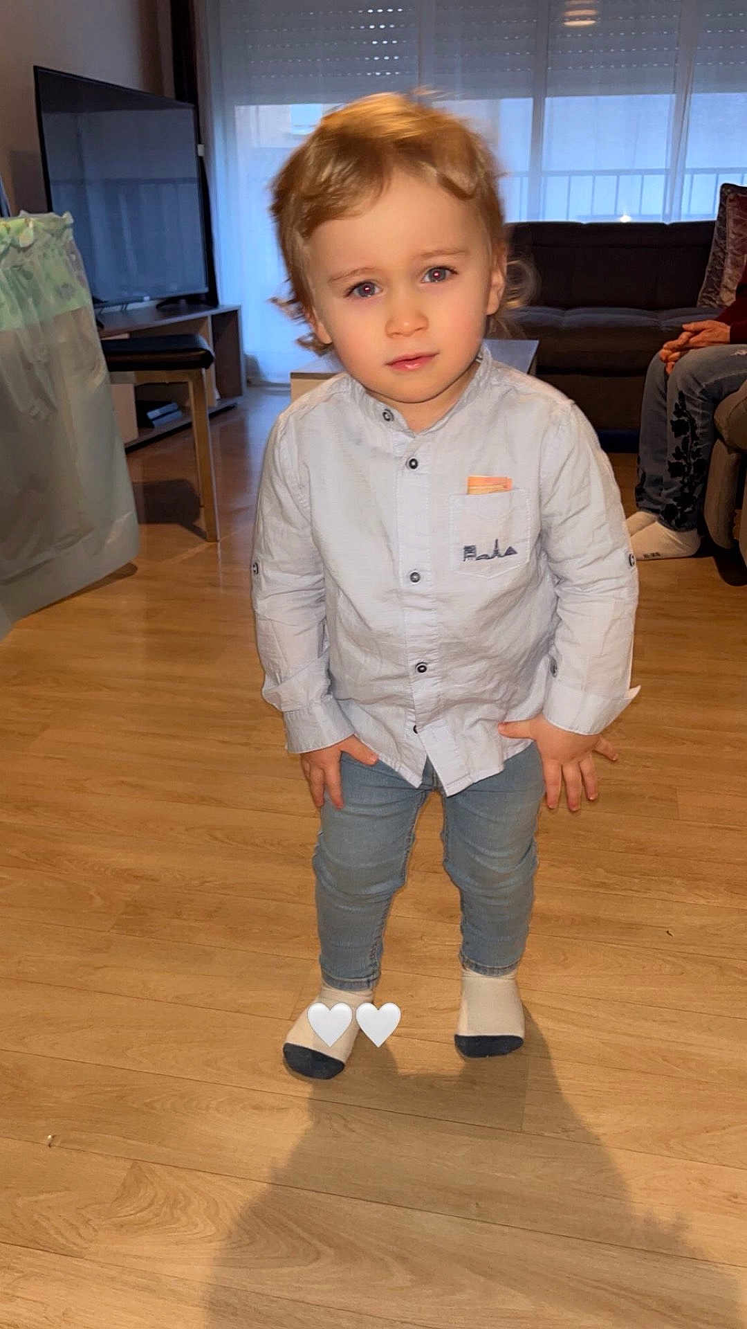 Nael participe au concours pour gagner de l'argent avec cette photo : toddler, child, indoor, living_room, person, shirt, jeans, socks, floor, television, couch, furniture, curly_hair, standing, expression, hands, light, home, casual_clothing, privacy