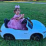 toddler, child, pink_dress, bow, toy_car, white_car, grass, outdoor, happy, clapping, green_lawn, suburban, smiling, cute, play, vehicle, sunlight, park, small_car, dress_up
