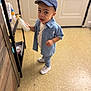 child, toddler, denim_shirt, cap, indoor, lotion_bottle, curious, standing, white_shoes, floor, door, shelf, clothing, person, young, casual_wear, expression, looking_up, home, small