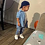 toddler, child, denim_shirt, jeans, sneakers, cap, basketball, indoor, wooden_floor, shadow, wall, chair, smiling, side_view, flooring, person, young_child, casual_clothing, happy, home_interior
