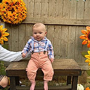 Julius is registered to the contest to win money with this photo: baby, child, bench, outdoor, plaid_shirt, suspenders, wooden_fence, sunflower_wreath, pumpkin, grass, blanket, autumn, fall, cute, person, hand, plaid, pants, shirt, smile