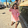 autumn, boots, buildings, child, daytime, fence, girl, heart_shaped, leaves, outdoor, pink_dress, portrait, sidewalk, smiling, strawberry_pattern, sunglasses, sunlight, tree, urban, water_bottle