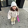building, child, coat, cute, daytime, door, glass, happy, hat, outdoor, pants, person, pink_purse, reflection, sidewalk, smile, sneakers, urban, winter_clothing, young