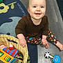 baby, child, smiling, toy, basket, floor, rug, colorful, indoor, clothing, patterned_pants, blue_eyes, happy, sitting, playtime, cute, infant, hand, foot, wooden_floor