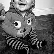 Archie is registered to the contest to win money with this photo: baby, black_and_white, child, clothing, cute, expression, eyes, face, floor, hand, happy, hoodie, indoor, infant, person, portrait, sitting, smiling, striped_socks, wooden_floor