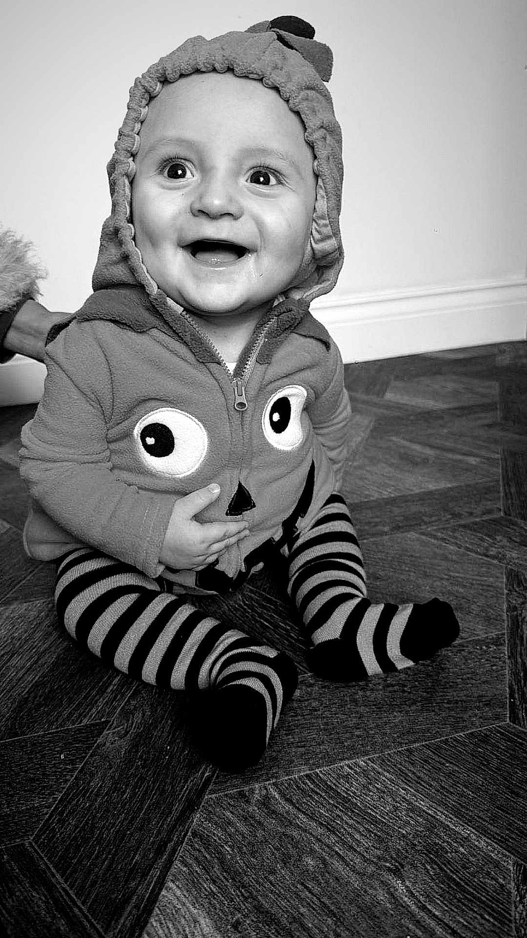 Archie is registered to the contest to win money with this photo: baby, black_and_white, child, clothing, cute, expression, eyes, face, floor, hand, happy, hoodie, indoor, infant, person, portrait, sitting, smiling, striped_socks, wooden_floor