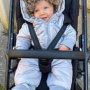 Avön a rejoint le concours — aidez-le/la à gagner de superbes lots ! baby, stroller, winter_clothing, snowsuit, hood, fur_trim, blue_eyes, smile, infant, child, outdoor, seatbelt, black_stroller, cute, cold_weather, jacket, mittens, happy, person, portrait