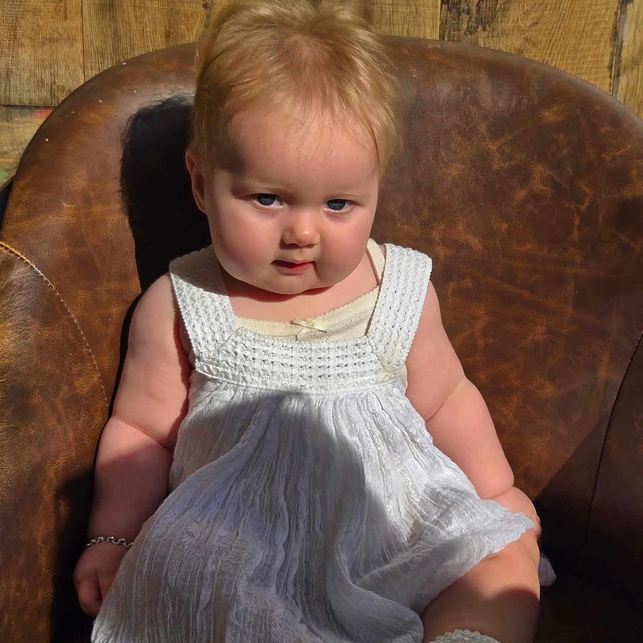 Amora-Louise is registered to the contest to win money with this photo: baby, bracelet, candid, child, cute, face, indoors, infant, leather_chair, plush, portrait, seated, serious_expression, shadow, short_hair, skin, socks, sunlight, white_dress, wooden_background