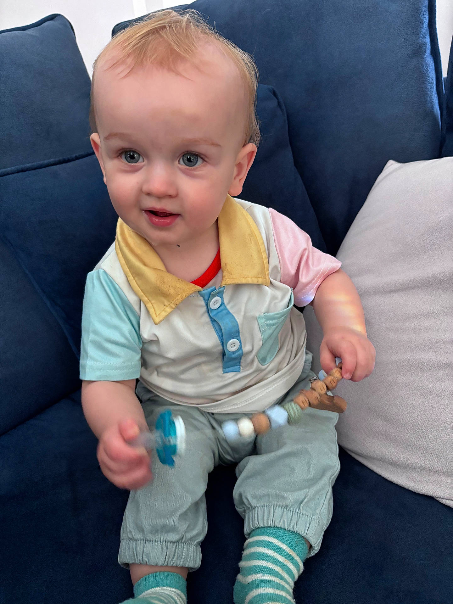baby, blue_couch, casual, child, colorful_clothing, cute, furniture, happy, indoor, pacifier, person, pillow, playful, portrait, seated, smiling, striped_socks, toddler, toy, young_child