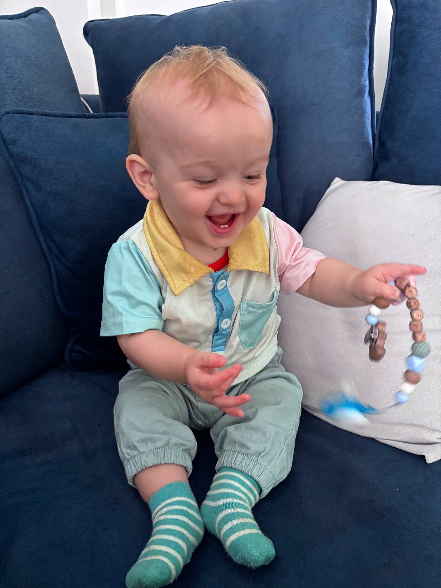 baby, beads, casual, child, clothing, couch, fabric, face, furniture, hair, hands, happy, indoor, person, pillow, playful, sitting, smiling, striped_socks, toy