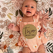 Julia joined the competition — help win amazing prizes! baby, infant, two_months, milestone, smiling, floral, blanket, romper, pink, daisies, wooden_sign, prop, face, eyes, hands, legs, lying_down, portrait, cute, cozy