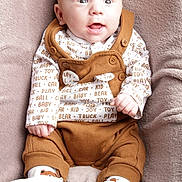 Hugo a rejoint le concours — aidez-le/la à gagner de superbes lots ! baby, infant, child, overalls, brown_clothing, white_booties, plush_blanket, seated, happy, wide_eyes, cute, portrait, indoor, soft_texture, clothing_pattern, small_hands, smiling, face, person, cozy