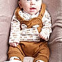 baby, infant, child, overalls, brown_clothing, white_booties, plush_blanket, seated, happy, wide_eyes, cute, portrait, indoor, soft_texture, clothing_pattern, small_hands, smiling, face, person, cozy