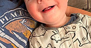 Noah is registered to the contest to win money with this photo: adult, animal_print, baby, child, close_up, clothing, couch, eyes, face, happy, home, indoor, infant, onesie, outdoorless, parent, portrait, sitting, smiling, toys