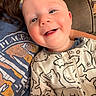 Noah is registered to the contest to win money with this photo: baby, child, infant, smiling, happy, portrait, close_up, face, eyes, outdoorless, indoor, sitting, clothing, onesie, animal_print, adult, parent, couch, home, toys