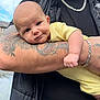 baby, infant, tattoo, arm, yellow_onesie, chain, black_jacket, outdoor, sky, house, person, holding, cute, face, expression, skin, hand, portrait, closeup, smile