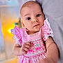 baby, bed, big_eyes, child, close_up, cozy, curious, cute, embroidery, fabric, face, hand, indoors, infant, pink_dress, portrait, sleepwear, soft_lighting, striped_clothing, young_child