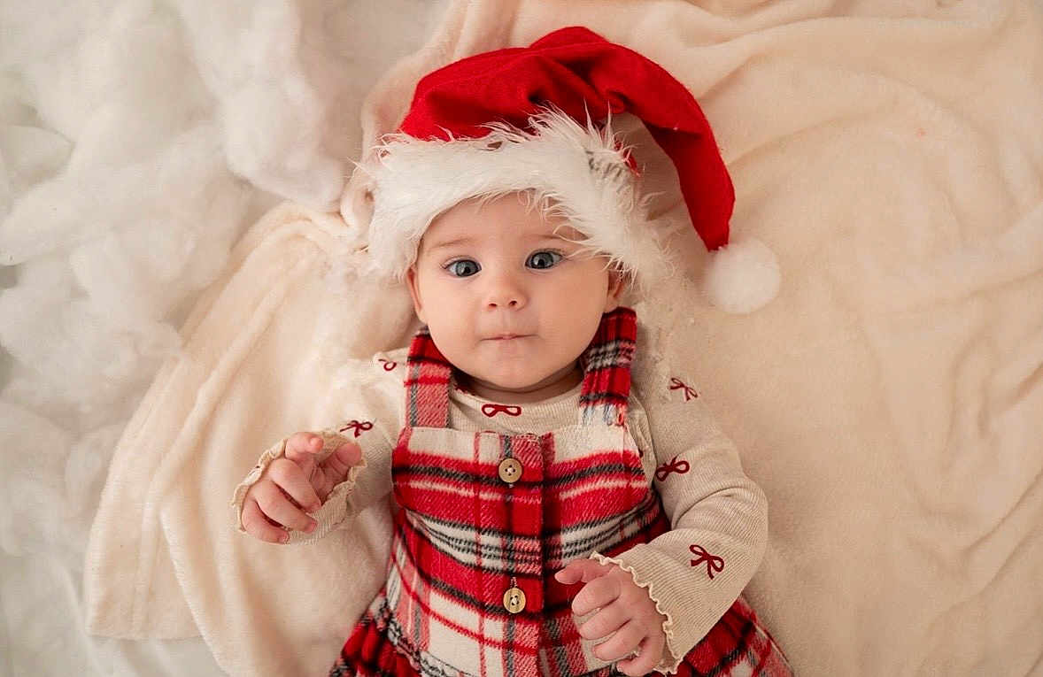 Pippa is registered to the contest to win money with this photo: baby, blanket, child, christmas, cozy, cute, face, festive, hands, holiday, indoors, infant, laying_down, plaid_dress, portrait, red_clothing, santa_hat, smiling, soft_texture, winter