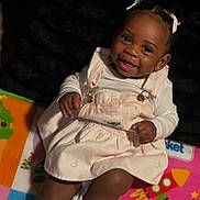 Janiyah Rhodes is registered to the contest to win money with this photo: baby, child, infant, smiling, portrait, sitting, indoor, play_mat, colorful, dress, overalls, sneakers, hair_bows, dark_skin, happy, playroom, toy_mat, closeup, feet, casual