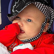 Galaxy Watts is registered to the contest to win money with this photo: baby, infant, face, hat, red_clothing, blanket, hand, sleeve, close_up, cute, child, portrait, skin, headwear, indoors, person, newborn, expression, apparel, young