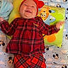 baby, smiling, red_clothing, plaid, headband, pillow, blanket, mickey_mouse, bed, infant, happy, child, indoors, cute, patterned_clothing, person, lying_down, soft_toys, colorful, playful
