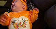 Galaxy Watts joined the competition — help win amazing prizes! baby, infant, smiling, orange_clothing, headband, couch, indoor, happy, cute, child, person, jeans, text_on_clothing, bee_graphic, portrait, sitting, bright_colors, playful, young_child, casual