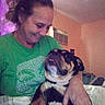 woman, dog, indoor, smile, green_shirt, air_conditioner, affection, pet, love, home, casual, portrait, human, animal, brown, black, tan, face, hand, comfort