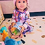 barefoot, child, colorful_clothing, couch, curious_look, cute, headband, home_environment, indoor, orange_toy, pajamas, patterned_floor, pink_bow, play_mat, plush_toy, sitting, soft_toys, toddler, toy_container, young_child
