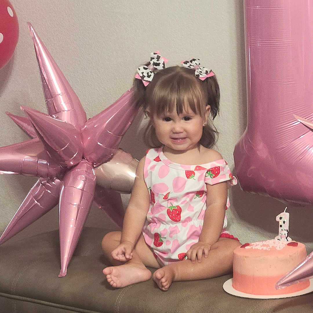 Alyanna is registered to the contest to win money with this photo: balloon, bench, birthday, bows, cake, celebration, child, cute, dress, girl, happy, indoor, number_one, party, pigtails, pink, portrait, smile, strawberry_pattern, toddler