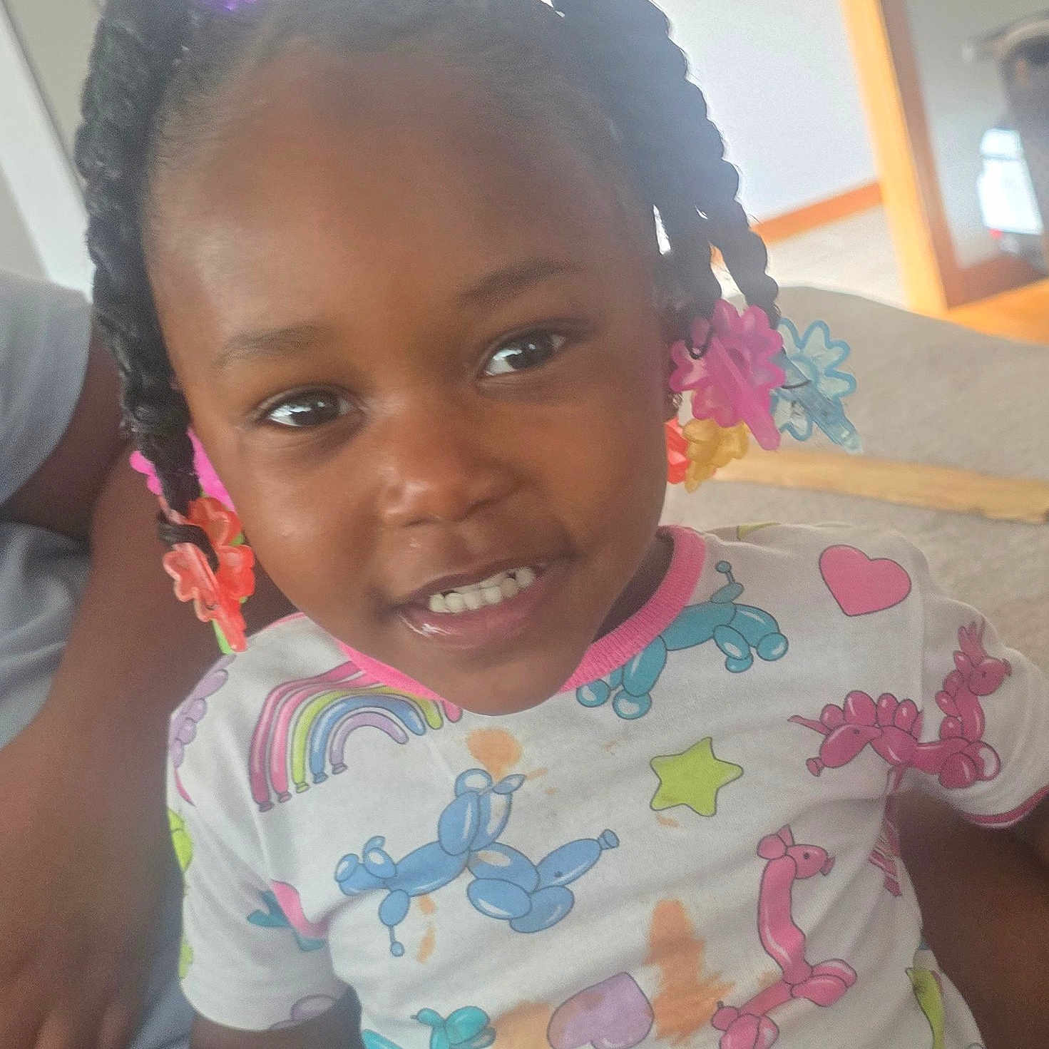 Yani is registered to the contest to win money with this photo: balloon_animal_print, braids, casual, child, clothing, colorful, cute, face, hair_accessories, happy, home, indoor, person, playful, portrait, seated, shirt, smiling, toddler, young_child