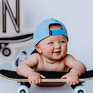 Jaxon is registered to the contest to win money with this photo: baby, child, skateboard, blue_cap, drool, smiling, cute, indoor, portrait, baby_skin, playful, headwear, toy, cheeks, hands, looking_away, happy, young_child, infant, casual