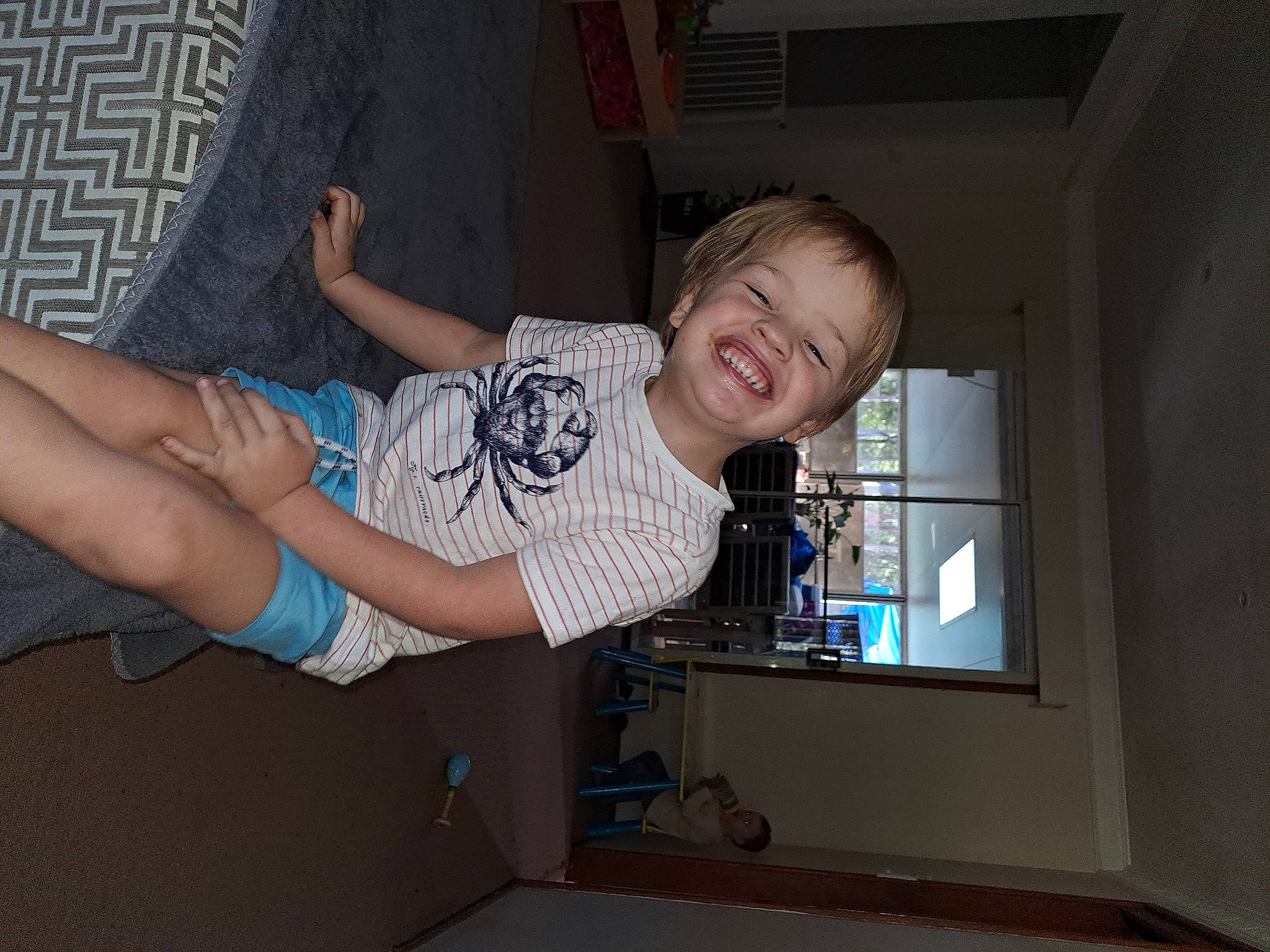 Owen is registered to the contest to win money with this photo: child, elbow, finger, foot, fun, gesture, happy, human_leg, joint, joy, knee, person, room, shorts, smile, t_shirt, thigh, thumb, toddler, under_exposed
