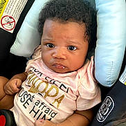 Ziella is registered to the contest to win money with this photo: baby, infant, child, car_seat, pink_shirt, curly_hair, face, eyes, hands, clothing, seatbelt, safety, cute, portrait, expression, indoor, young_child, person, head_support, car_interior