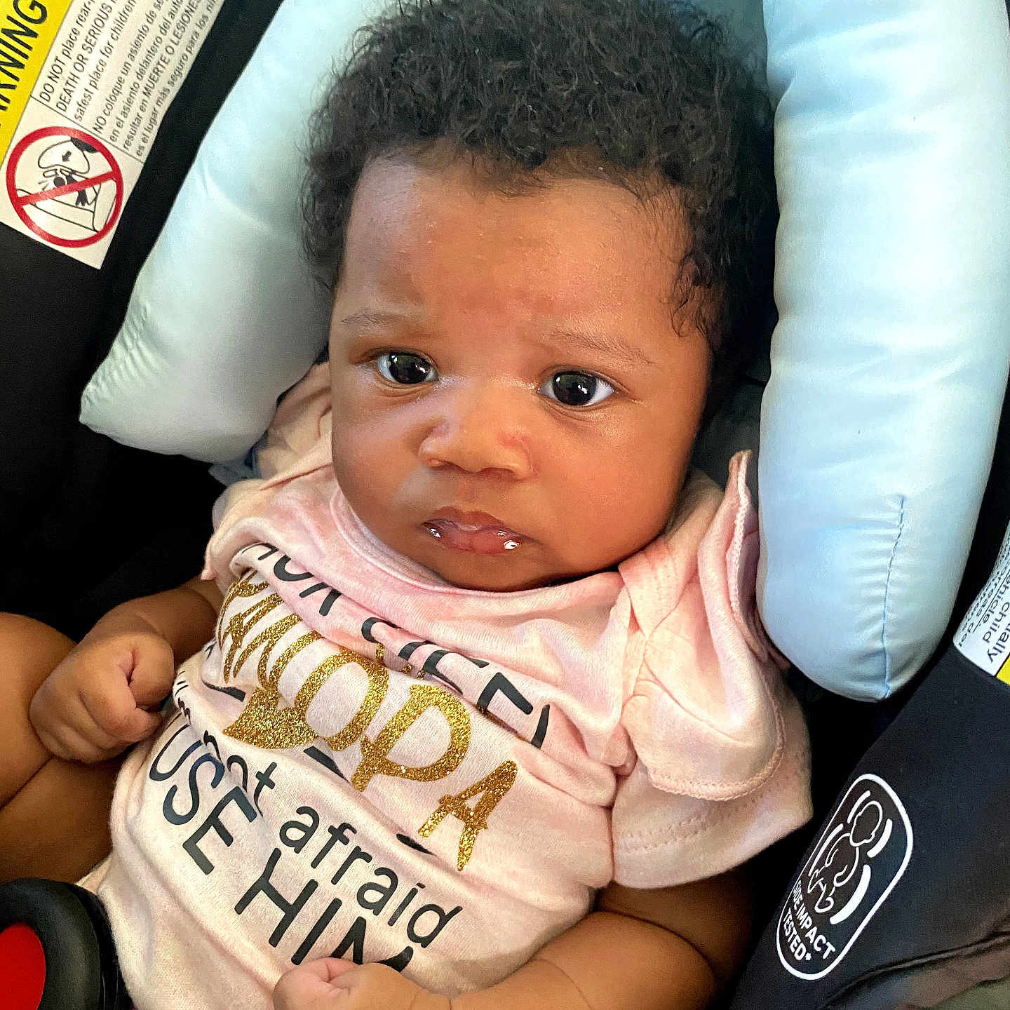 Ziella is registered to the contest to win money with this photo: baby, infant, child, car_seat, pink_shirt, curly_hair, face, eyes, hands, clothing, seatbelt, safety, cute, portrait, expression, indoor, young_child, person, head_support, car_interior