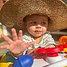 Braxton joined the competition — help win amazing prizes! toddler, child, hat, sun_hat, toy, activity_table, hand, face, striped_shirt, outdoor, sunlight, shadow, playful, curious, baby, young_child, colorful, closeup, expression, portrait