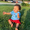 Braxton is registered to the contest to win money with this photo: barefoot, blue_shirt, casual_clothing, child, curious, daytime, grass, greenery, happy, nature, outdoor, person, playful, red_shorts, shadow, sitting, suburb, summer, sunlight, toddler