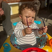 Braxton is registered to the contest to win money with this photo: toddler, baby, sunglasses, walker, outdoor, sunlight, curious, striped_shirt, toy, face, person, dog, blurred_background, hand, expression, seat, playtime, child, daylight, exploration