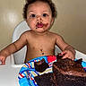 birthday_cake, brown_skin, cake, celebration, child, chocolate, curly_hair, dessert, expression, food, hands, happy, high_chair, indoor, messy_face, person, plate, sitting, snack, toddler