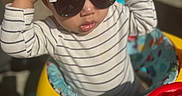 Braxton joined the competition — help win amazing prizes! toddler, child, baby_walker, sunglasses, striped_shirt, curly_hair, indoor, colorful, toy, hands_up, playtime, cute, person, young_child, fashion, headwear, seat, bright_colors, baby, fun
