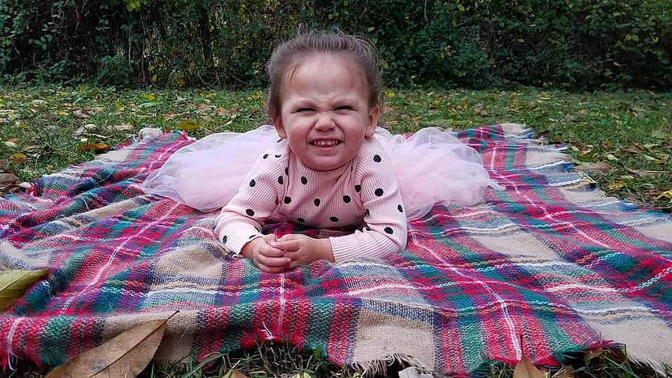 Cecilia is registered to the contest to win money with this photo: child, facial_expression, fun, girl, grass, infant, joy, pattern, person, picnic, pink, plaid, plant, play, recreation, sitting, smile, textile, toddler, tree