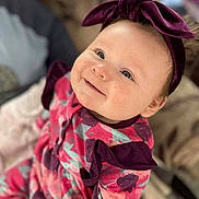 Emily is registered to the contest to win money with this photo: baby, child, smile, headband, purple_bow, floral_outfit, indoor, portrait, cute, infant, person, happy, young_child, cozy, soft_focus, apparel, fashion, sitting, bright_eyes, closeup