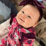 baby, child, smile, headband, purple_bow, floral_outfit, indoor, portrait, cute, infant, person, happy, young_child, cozy, soft_focus, apparel, fashion, sitting, bright_eyes, closeup