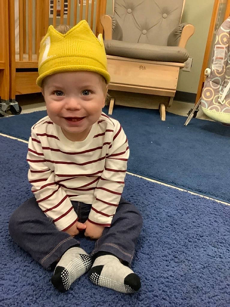 Mason is registered to the contest to win money with this photo: baby, baby_toddler_clothing, cap, carpet, child, costume_hat, floor, flooring, foot, fun, happy, headwear, joy, person, room, sitting, sleeve, smile, toddler, wood
